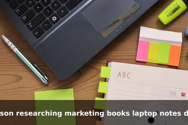 person researching marketing books laptop notes desk
